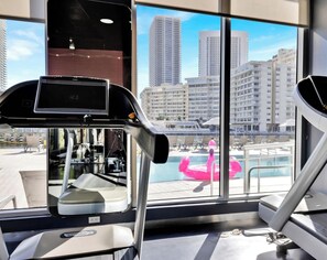 Ein Fitnessraum mit Trainingsgeräten und einem großen Fenster mit Blick auf die Stadt.