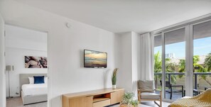 A modern hotel room with a bed, a TV, a balcony with a view, and a wooden console table. - Luxury 1BR - Bay View - Beachwalk Beach Resort (Hallandale Beach)