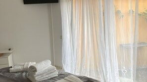 A hotel room with a bed, a bedside table, a TV mounted on the wall, and sheer curtains over a window. - Beautiful Bungalow for Families with Private Entrance (Weilerswist)