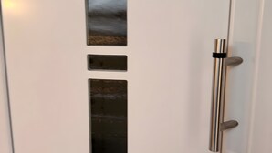 Une porte blanche dotée d’une poignée métallique verticale et de trois panneaux métalliques rectangulaires.