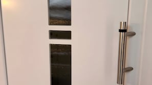 Une porte blanche dotée d’une poignée métallique verticale et de trois panneaux métalliques rectangulaires.