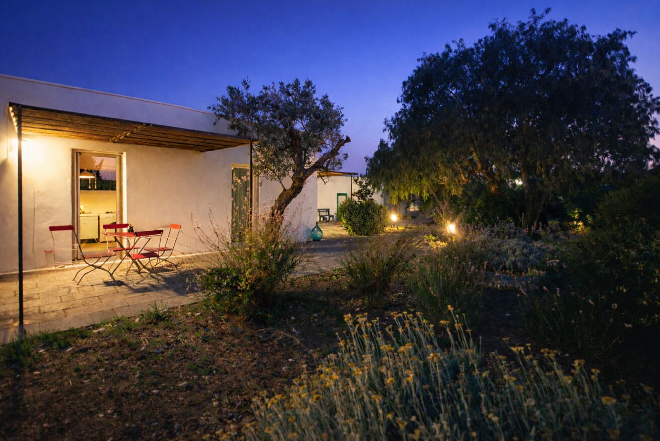 Una casa moderna con patio, mobiliario exterior y jardín al anochecer.
