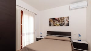 Une chambre à coucher comprenant un lit, une table de chevet, un climatiseur fixé au mur et une fenêtre avec des rideaux.