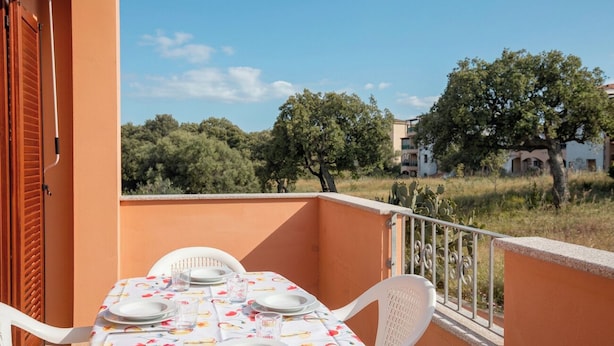 Un balcon avec une table dressée pour quatre personnes, des chaises blanches et une balustrade.