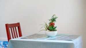 Une table recouverte d’une nappe bleue, un bol blanc contenant une plante et une chaise rouge.