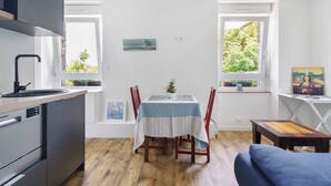 Une cuisine moderne dotée d’un lave-vaisselle intégré, d’une table à manger recouverte d’une nappe à rayures et offrant une vue sur la verdure par les fenêtres.