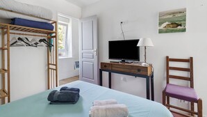 Une chambre à coucher avec un lit, un téléviseur posé sur une table en bois, une chaise et un tableau accroché au mur.