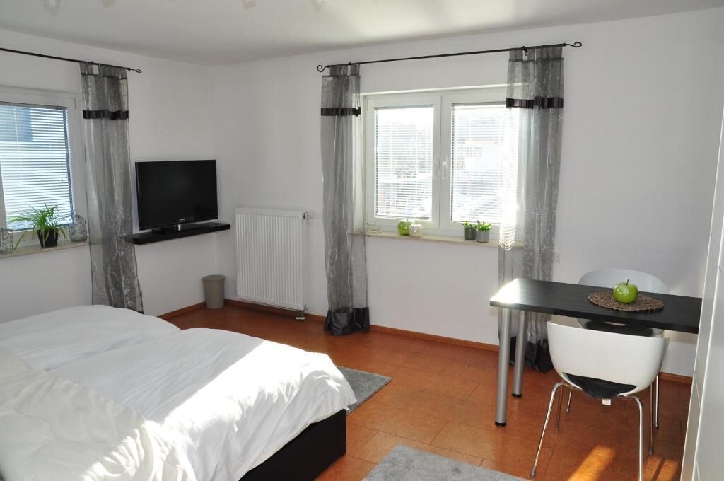 Een slaapkamer met een bed, een televisie, een bureau met stoel en een raam met gordijnen.