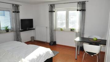 Een slaapkamer met een bed, een televisie, een bureau met stoel en een raam met gordijnen.