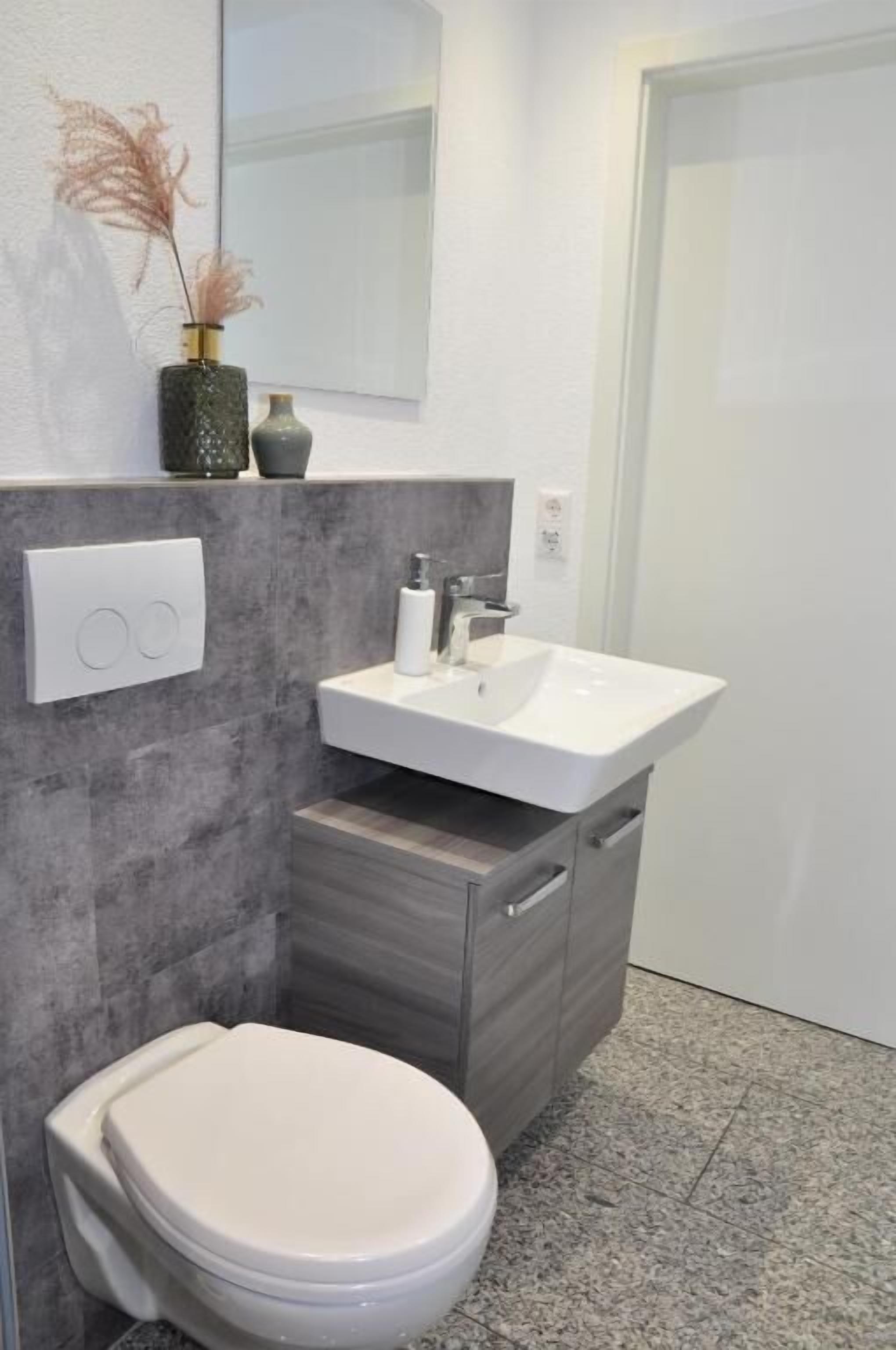 Un baño moderno con un inodoro blanco, un lavabo blanco y un espejo encima.