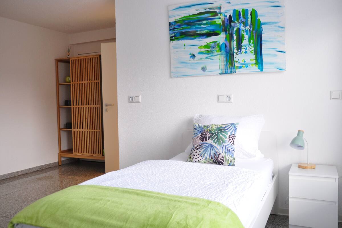 Un dormitorio con cama, mesita de noche, un cuadro en la pared y un armario de madera.