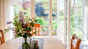 Een eettafel met stoelen, een vaas met bloemen en uitzicht op een tuin en een huis door grote ramen.