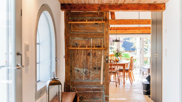 Een houten interieur met een landelijke deur, een eethoek met stoelen en een tafel, en uitzicht op het landschap door een glazen deur.