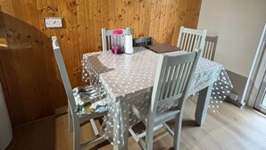 A dining area with a wooden wall, a table with a polka dot tablecloth, and two chairs. - Room-amina's Cottage Women Only Accommod (Gloucester)