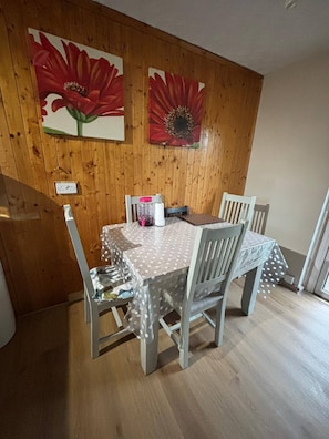 A dining area with a wooden wall, a table with a polka dot tablecloth, and two chairs. - Room-amina's Cottage Women Only Accommod (Gloucester)