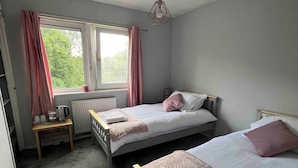A bedroom with two beds, a window with curtains, a radiator, and a table with a kettle. - Room-amina's Cottage Women Only Accommod (Gloucester)