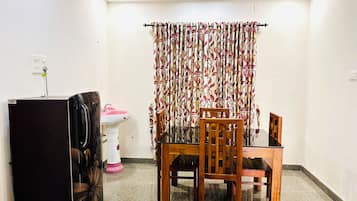 A room with a dining table, chairs, a refrigerator, a sink, and a curtain with a leaf pattern.