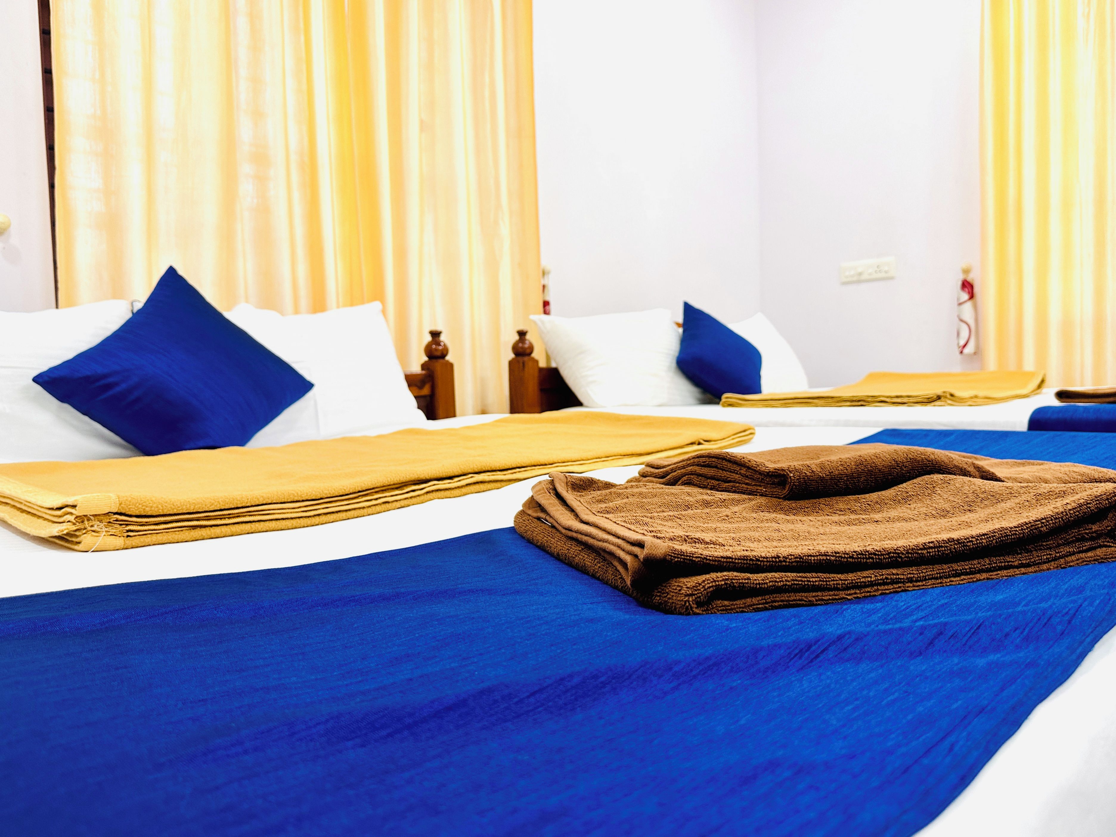 Habitación de hotel con dos camas, cada una con ropa de cama y almohadas azules, y una toalla marrón sobre la cama.