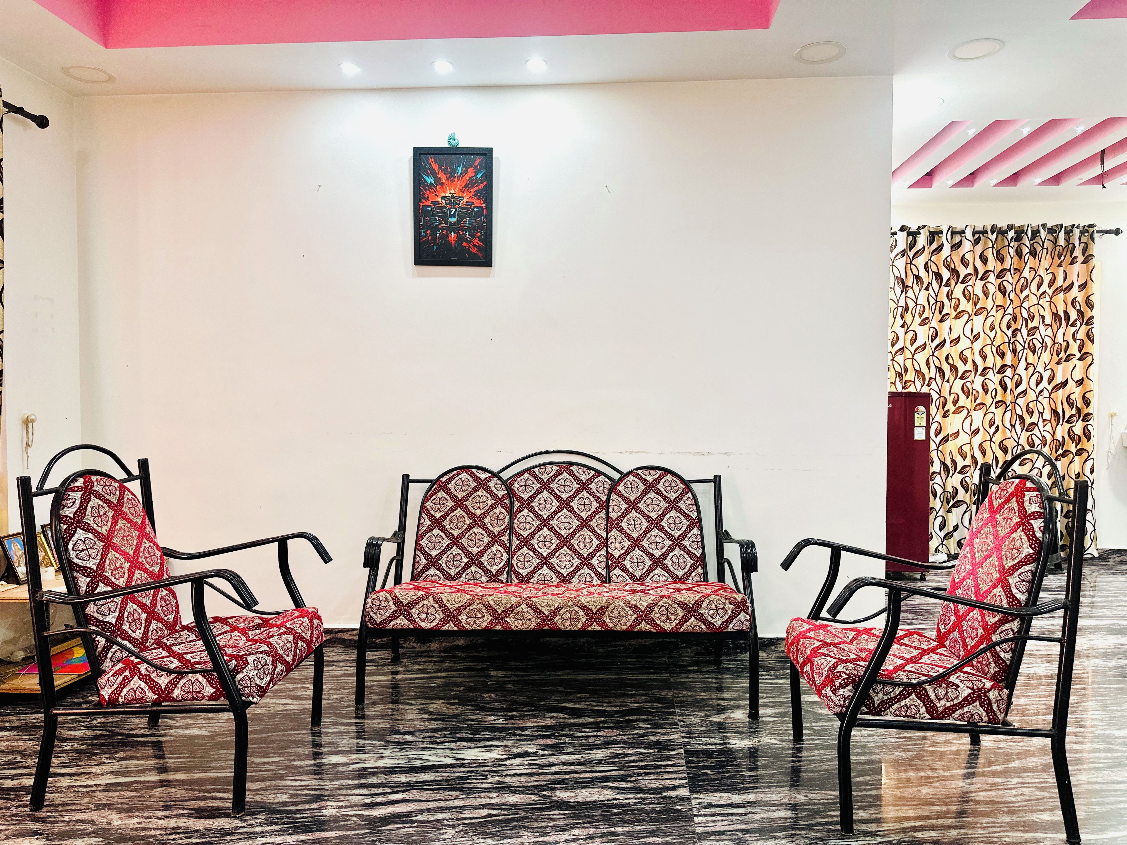 A room with a sofa and two chairs, a patterned curtain, and a framed picture on the wall.