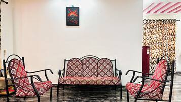A room with a sofa and two chairs, a patterned curtain, and a framed picture on the wall.