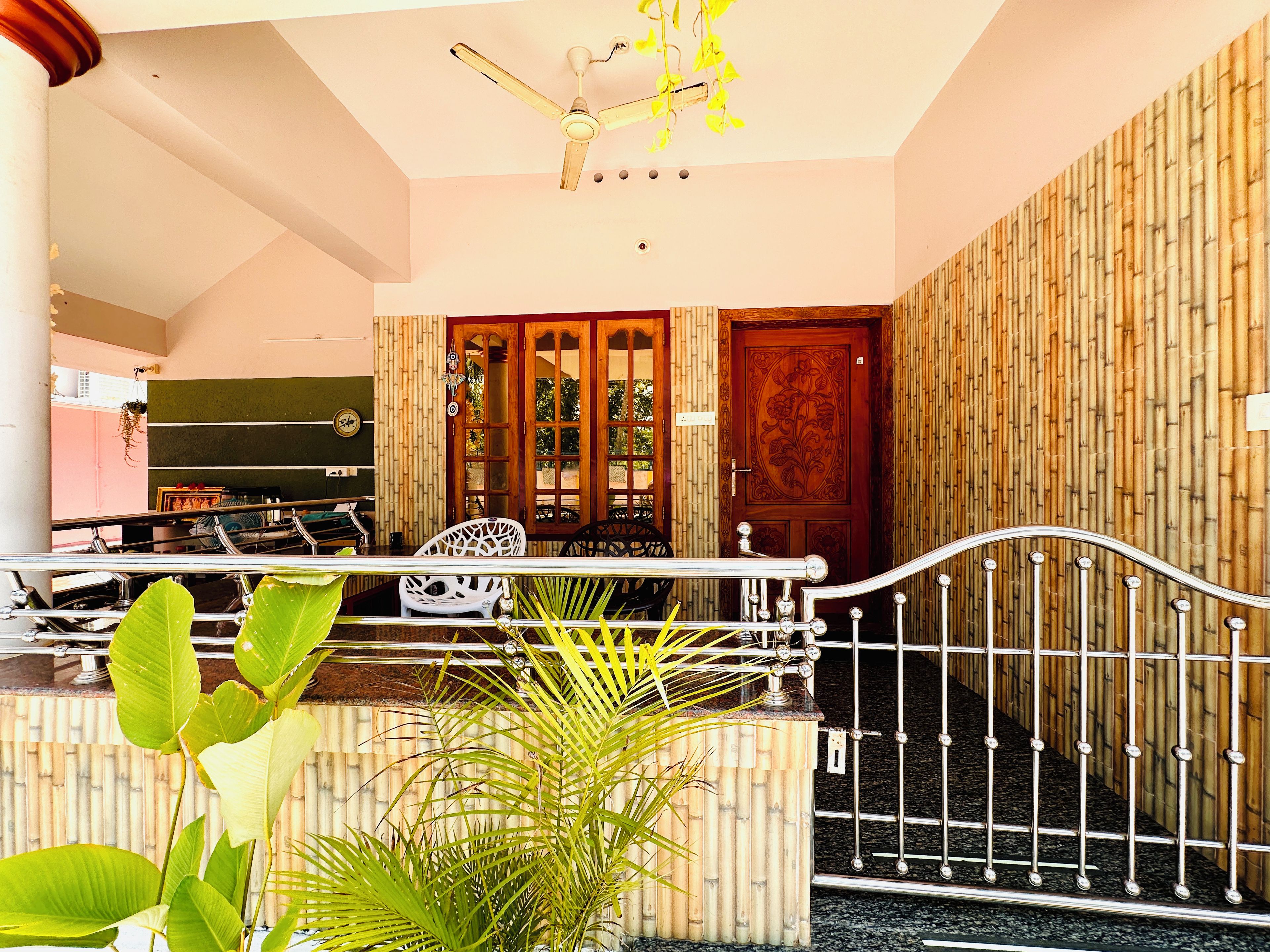 A room with a ceiling fan, a wooden door with intricate carvings, and a bamboo-patterned wall.
