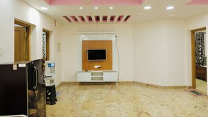 A room with a flat-screen TV mounted on a wooden panel, a water dispenser, a refrigerator, and a marble floor. - Varkala Breeze Villas (Varkala)