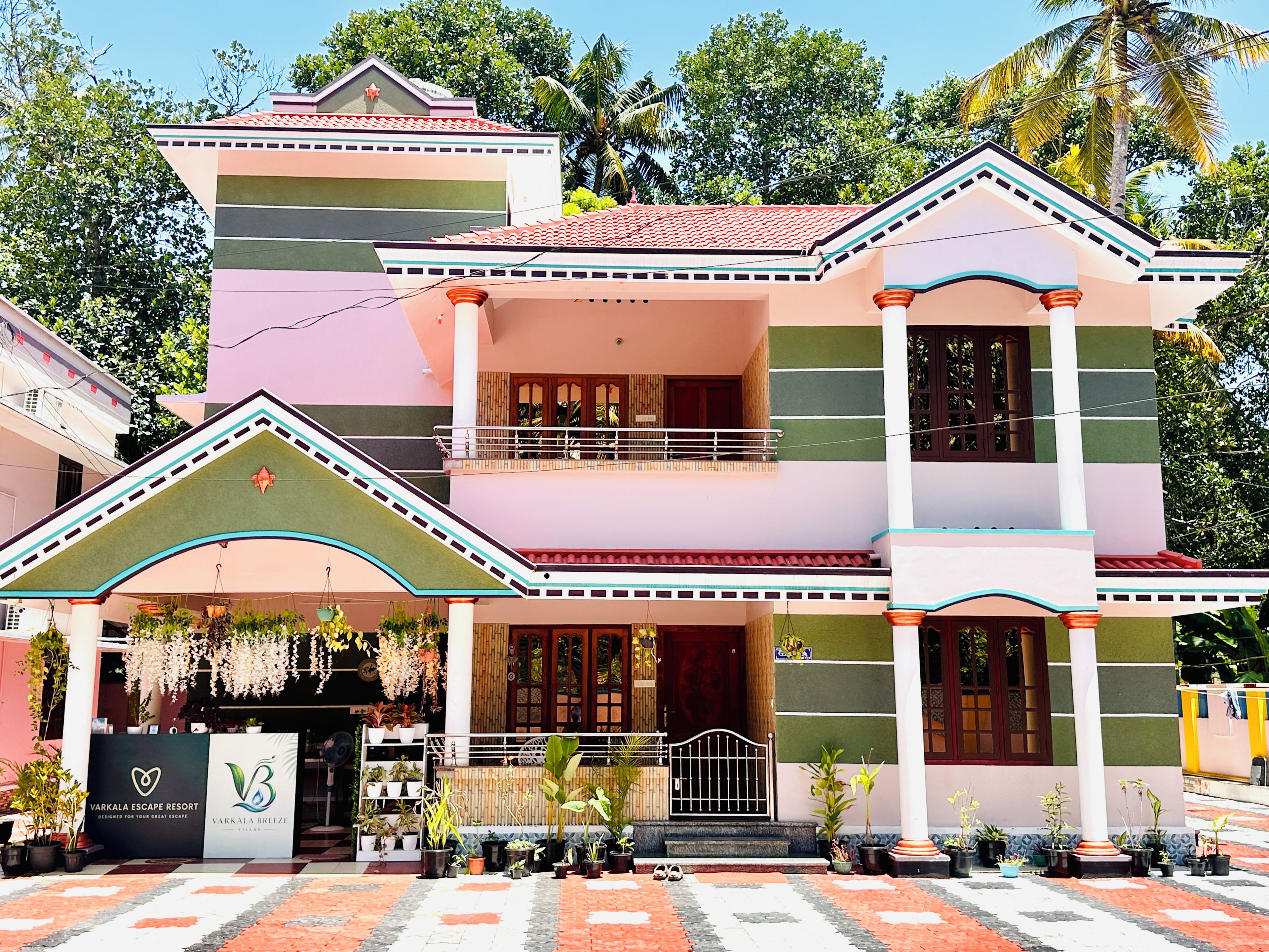 Un edificio de varios pisos con balcón, plantas en macetas y un letrero que indica Varkala Escape Resort.