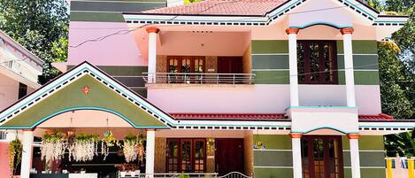 A multi-story building with a balcony, potted plants, and a sign for Varkala Escape Resort.