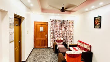 A hotel room with a wooden door, a ceiling fan, a patterned curtain, and a bed with a red and white quilt.