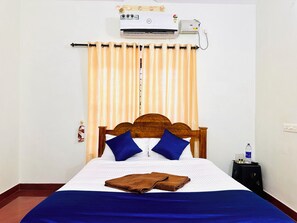 A hotel room with a bed, a wooden headboard, two blue pillows, a brown towel, and an air conditioning unit mounted on the wall. - Varkala Breeze Villas (Varkala)