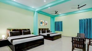 A hotel room with two beds, a desk, a chair, and a ceiling fan. - Rudraksh Residency (Varanasi)