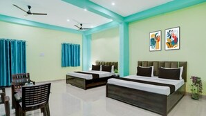A hotel room with two beds, a dining table with chairs, a ceiling fan, and artwork on the wall. - Rudraksh Residency (Varanasi)