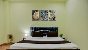 A hotel room with a bed, a nightstand, a lamp, and three framed artworks on the wall. - Rudraksh Residency (Varanasi)