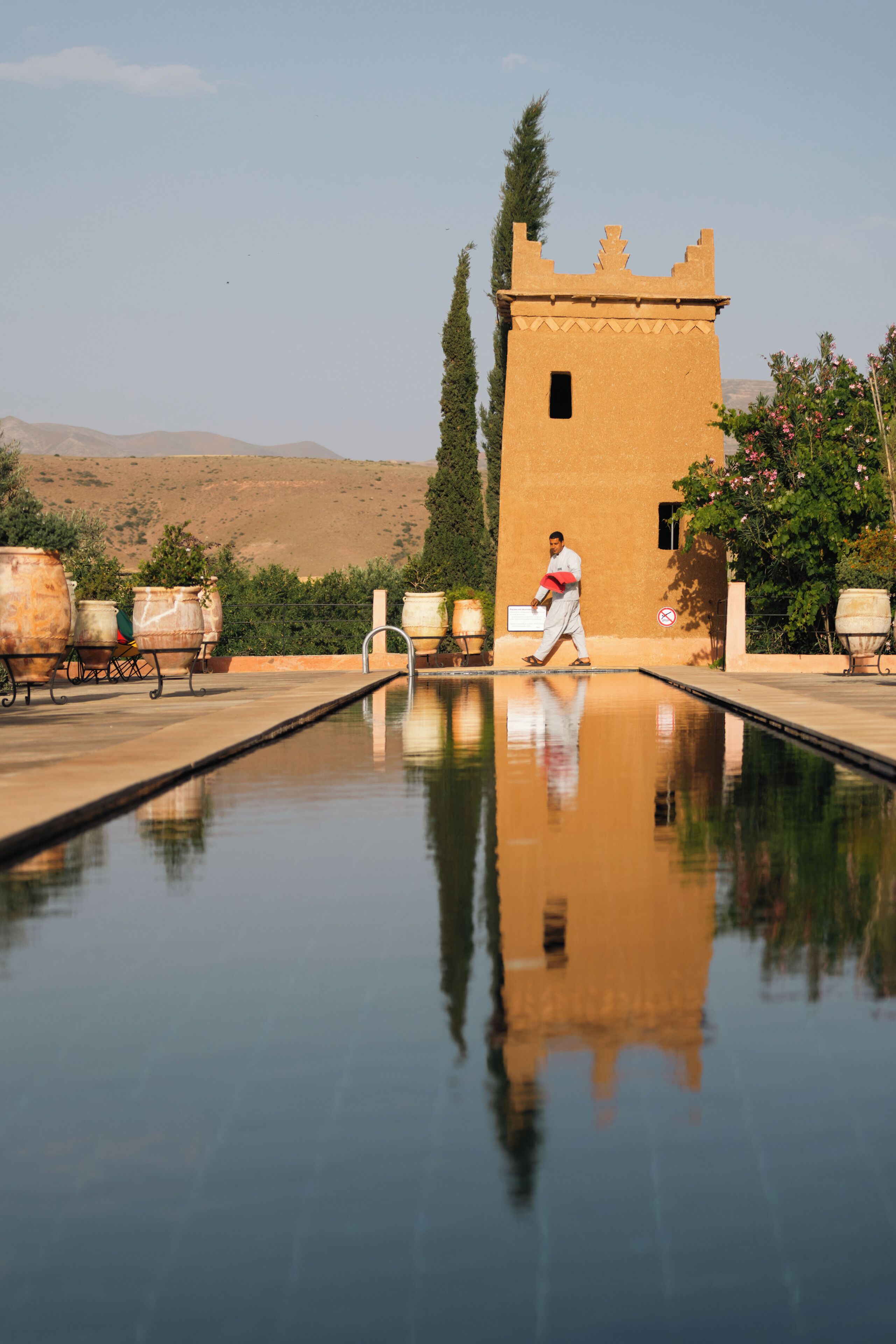 A man walking by a pool with a tower in the background.