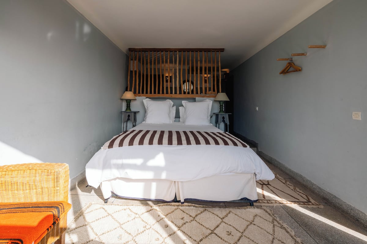 A bedroom with a bed, two bedside tables, a hanging light fixture, a wooden slat ceiling, and a patterned rug.