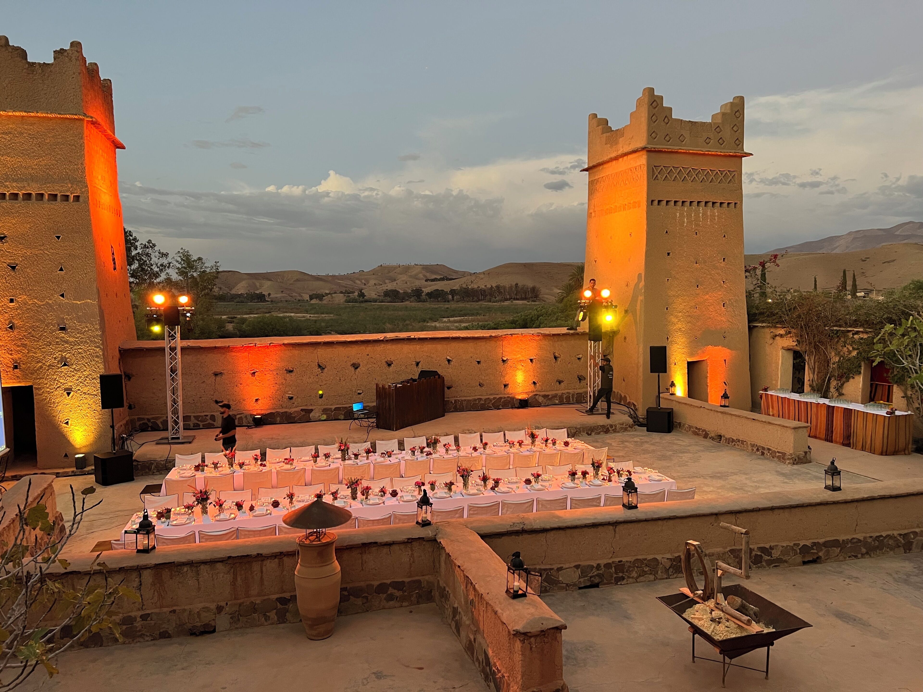 A courtyard with a stage, tables set for dining, and a view of the surrounding landscape.
