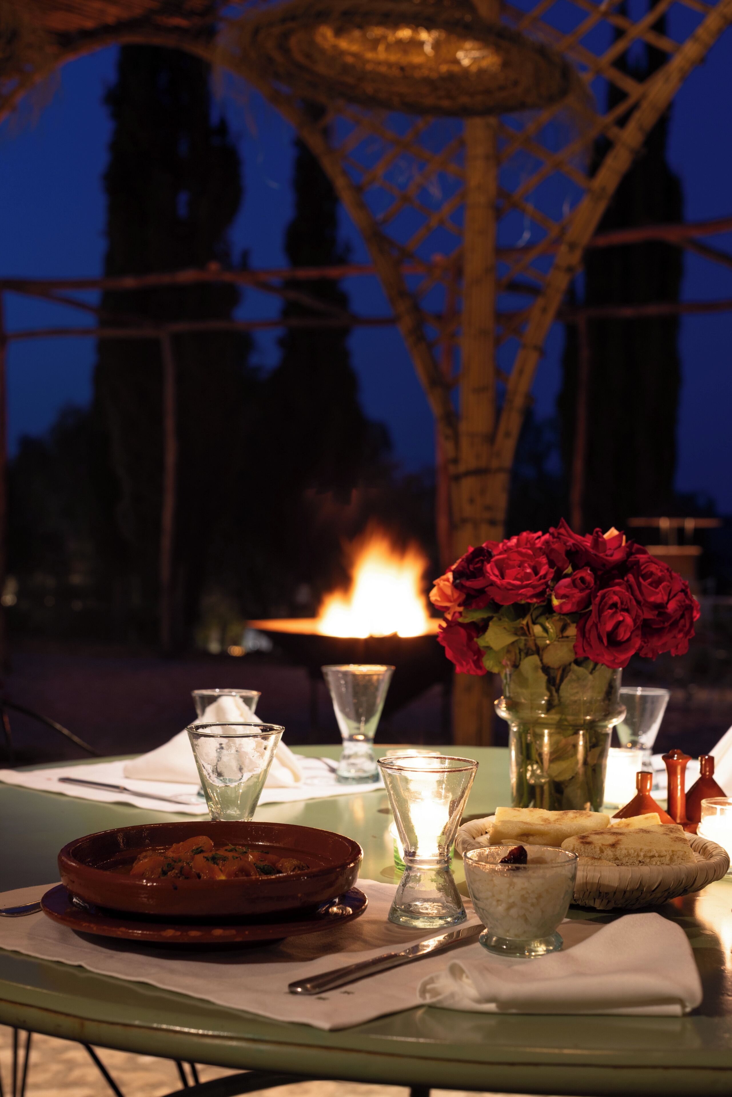 A table set for dining with a candle, a vase of roses, and a dish of food.