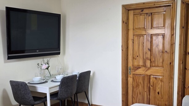 A room with a dining table set for four, a flat-screen TV mounted above it, and a wooden door. - Charming 2-bedroom Apartment in Dublin City Center (Dublin)