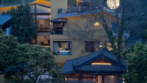 A multi-story building with traditional and modern architectural elements, surrounded by trees and hills. - Liaoxin Valley Forest Hotel (Chengdu)