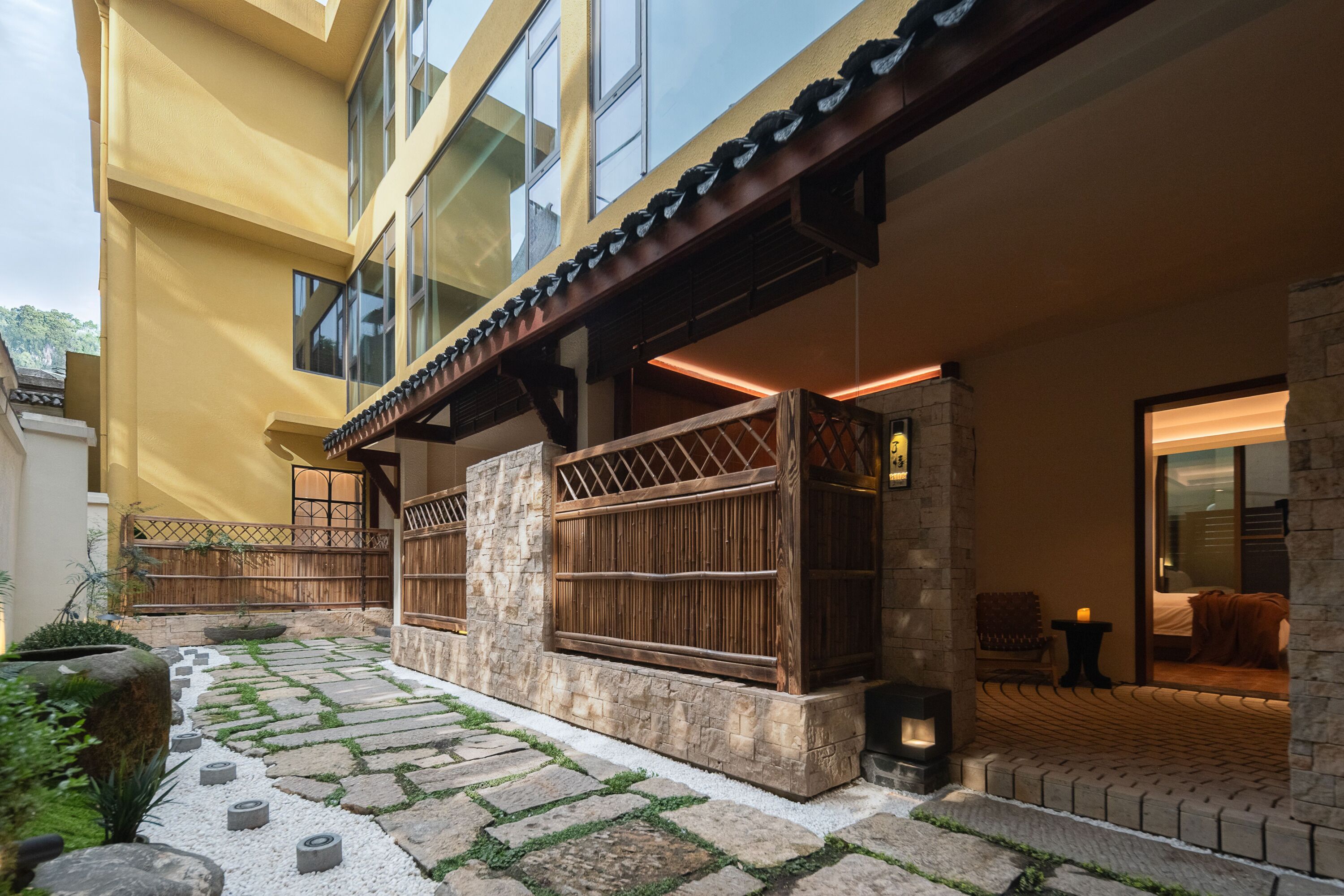 A building with a stone pathway, wooden fences, and a seating area with a table and chairs.