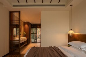 Une chambre d’hôtel comprenant un lit, une table de chevet, une lampe, une cloison en bois et donnant sur un balcon extérieur.