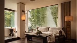 A modern living room with a sofa, a coffee table, a lamp, and a view of bamboo outside. - Liaoxin Valley Forest Hotel (Chengdu)