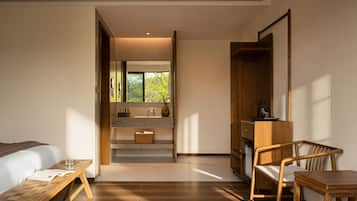 A modern hotel room with a bed, wooden bench, desk, and chair.