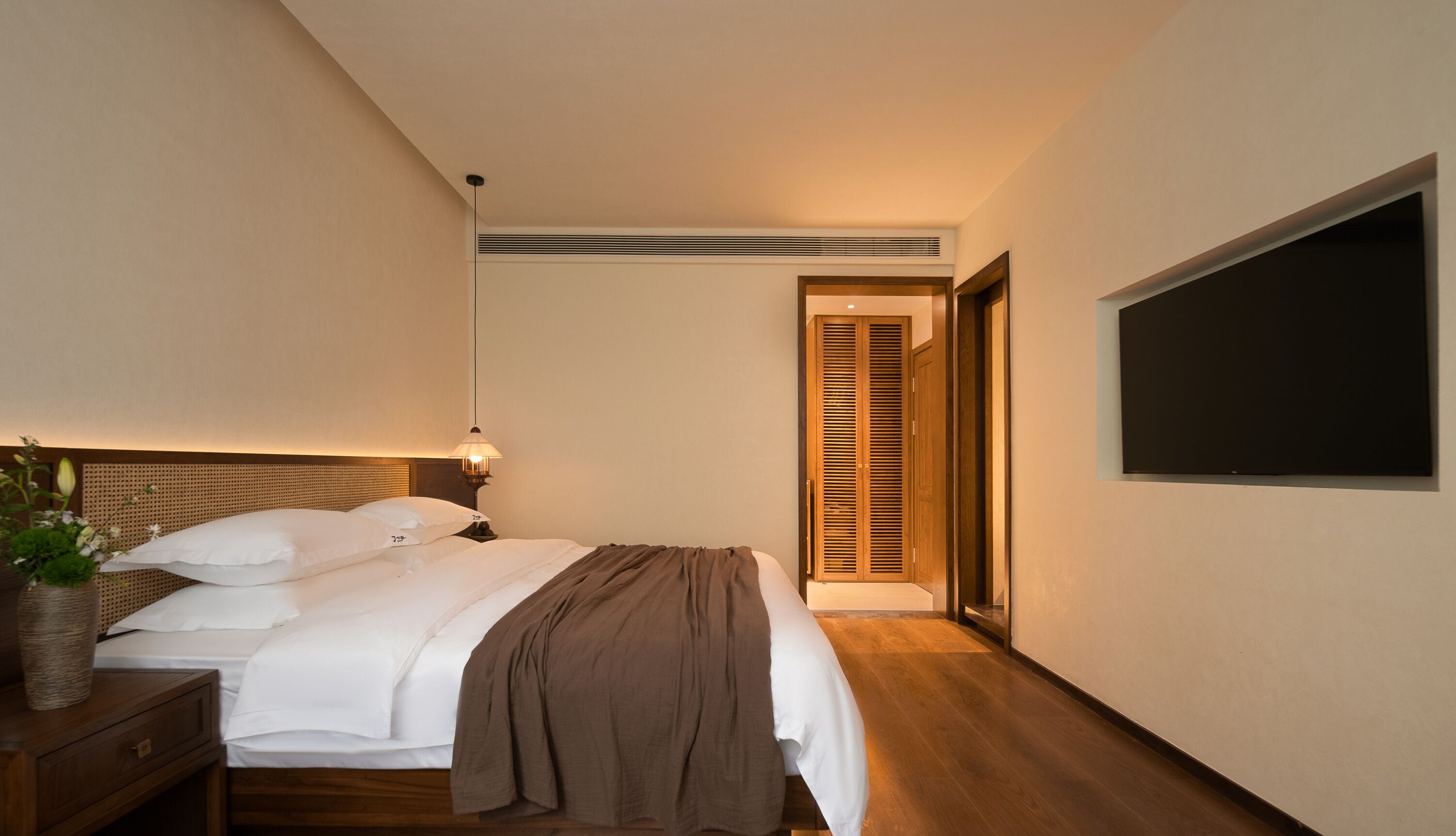 A hotel room with a bed, bedside table, lamp, and a TV mounted on the wall.