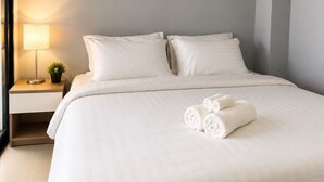 Una habitación de hotel moderna con una cama grande, una mesita de noche con lámpara y un equipo de aire acondicionado en la pared.