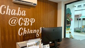 Mostrador de recepción con pared de madera, un monitor de computadora y un cartel con los precios de las habitaciones.
