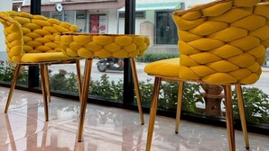Dos sillas amarillas de diseño peculiar, ubicadas frente a grandes ventanales con vista a un edificio.