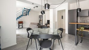 Eine moderne Küche mit einem eingebauten Kühlschrank, ein Essbereich mit einem Glastisch und schwarzen Stühlen sowie eine Treppe mit blauen Geländern.