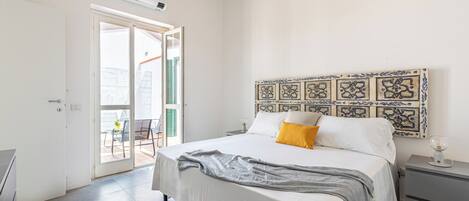 A bedroom with a bed, a nightstand, a decorative headboard, and a sliding glass door leading to an outdoor area.