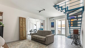 Ein Wohnzimmer mit einer Couch, einem gemusterten Teppich, einer Vintage-Nähmaschine und einer blauen Wendeltreppe.